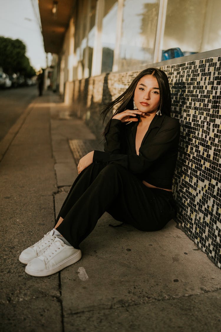 Young Model In A Black Blouse And Sweatpants Sitting On The Sidewalk