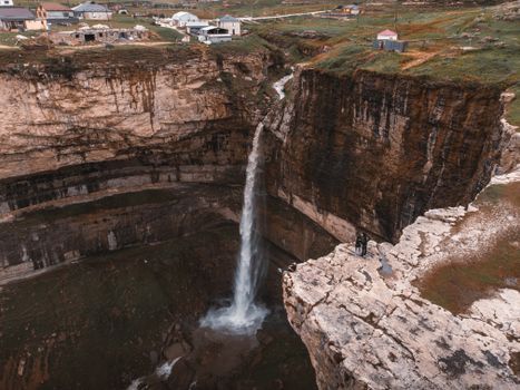 Breathtaking view of a waterfall cascading into a canyon with people at a cliffside viewpoint.