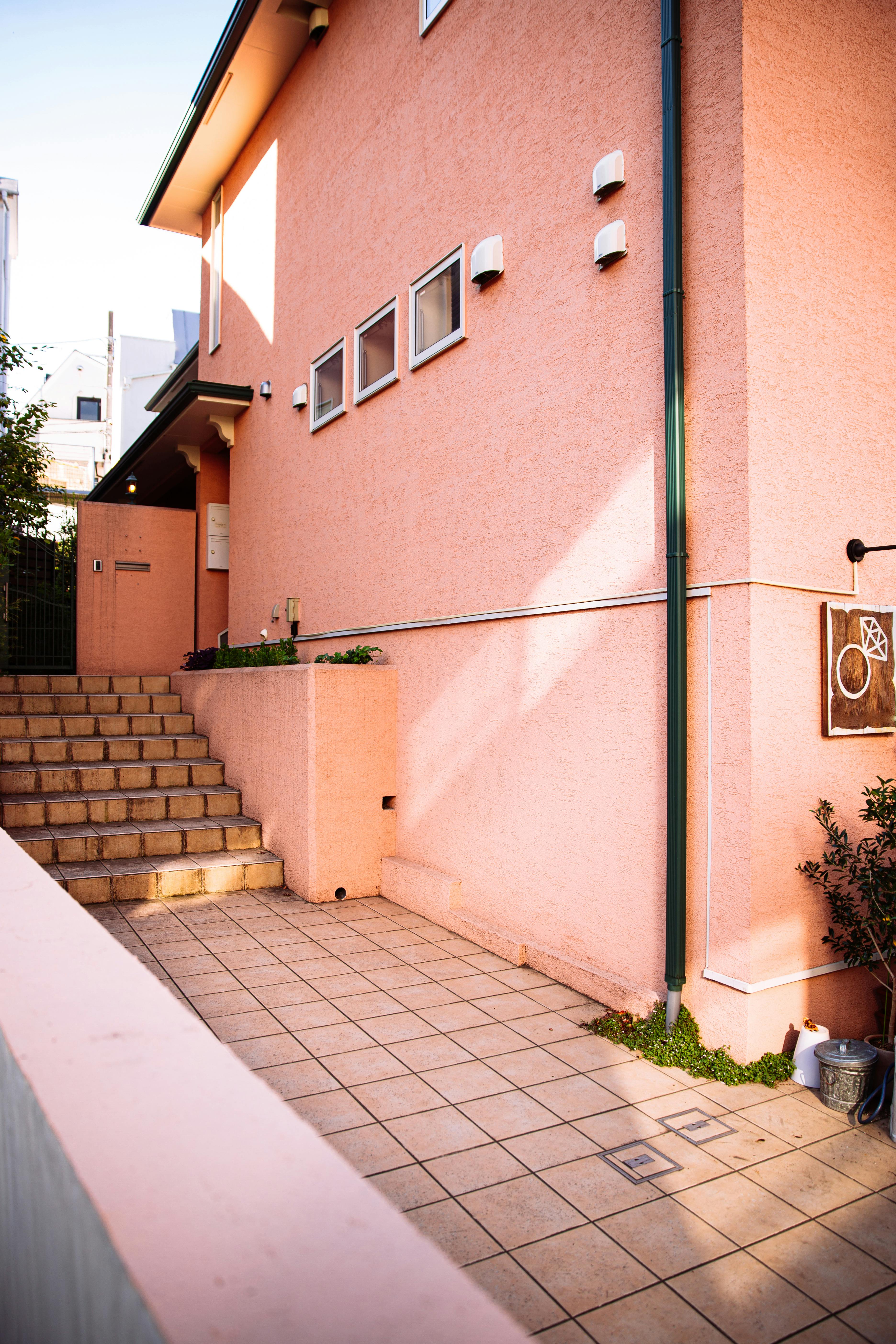 Explore a sunlit pink house exterior in Tokyo with vibrant steps and tiles.