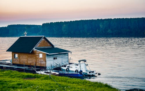 Kostenlos Weißes Boot Neben Holzhaus Auf Dem Wasser Nahe Wald Stock-Foto