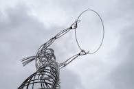 一座高大的抽象金属雕塑在多云的背景下向上延伸，展现了户外现代艺术的风采