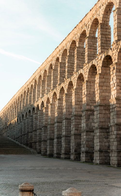 Free The ancient Roman Aqueduct of Segovia with its iconic arches glows in the warm sunset light. Stock Photo