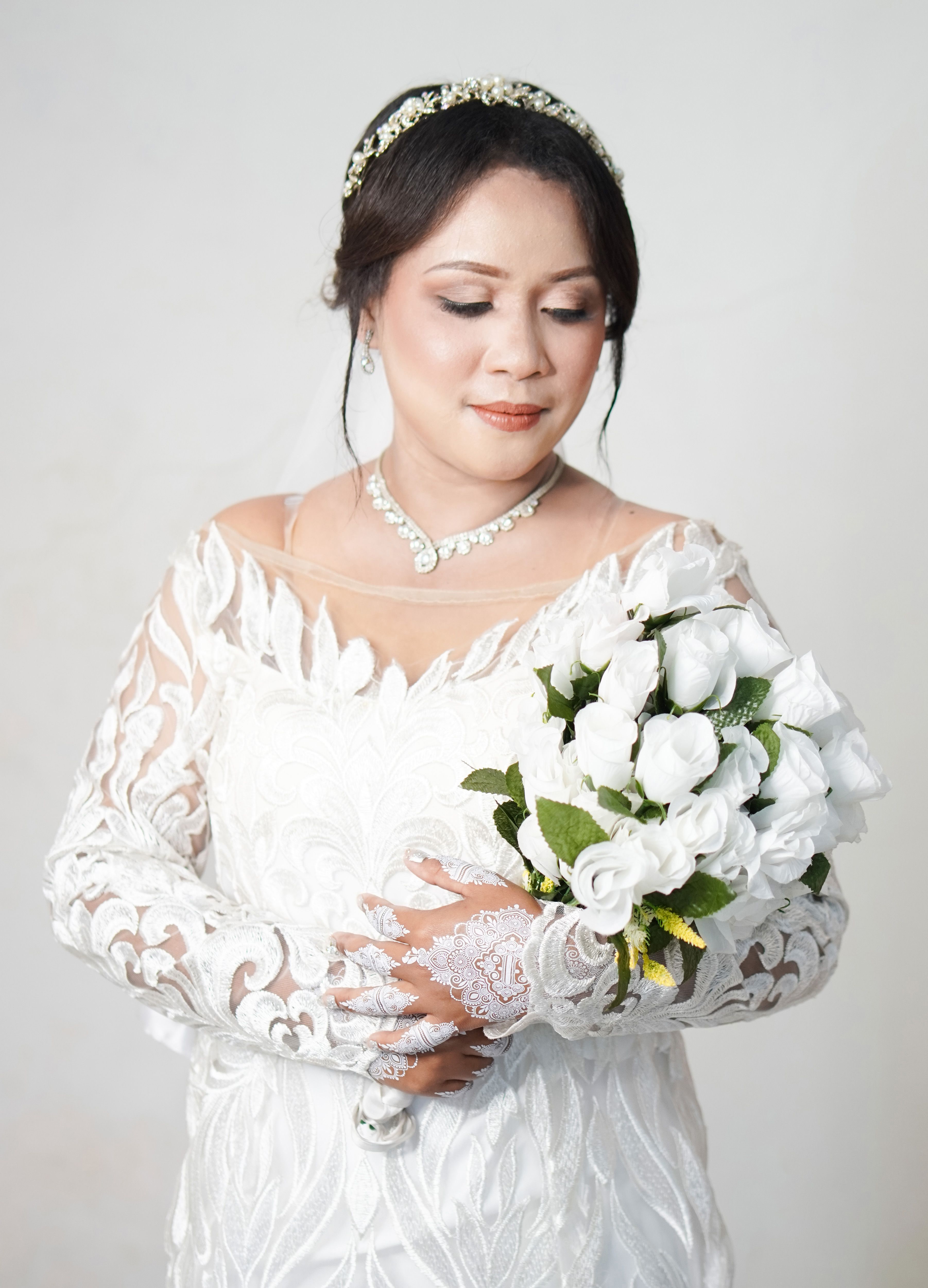 A beautiful bride in an elegant wedding dress holds a white rose bouquet, exuding grace and charm.