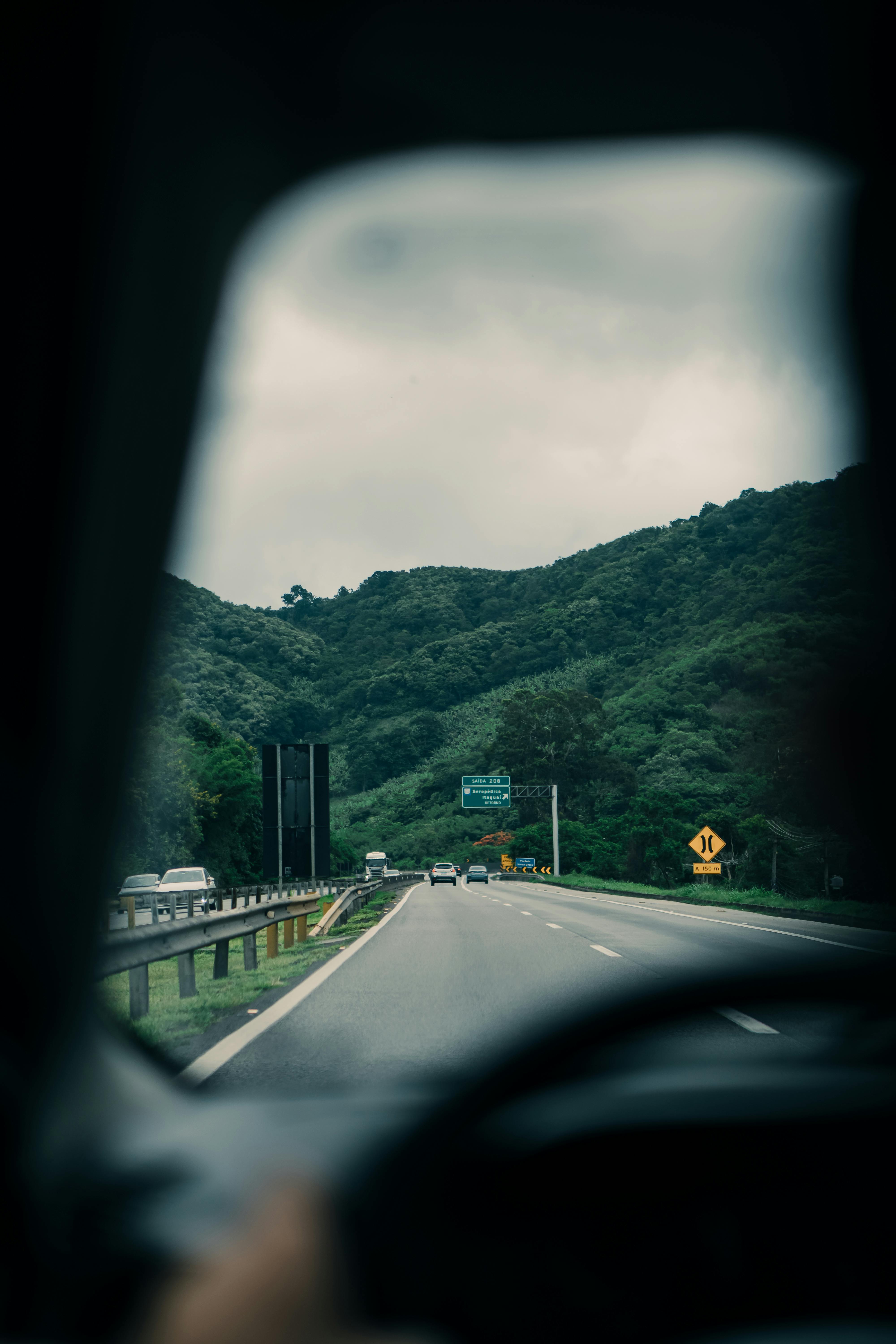 View through car window on a road trip through a lush green landscape, featuring distant hills and cloudy skies.