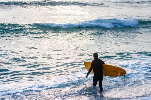 Man with a Yellow Surfboard Entering the Sea