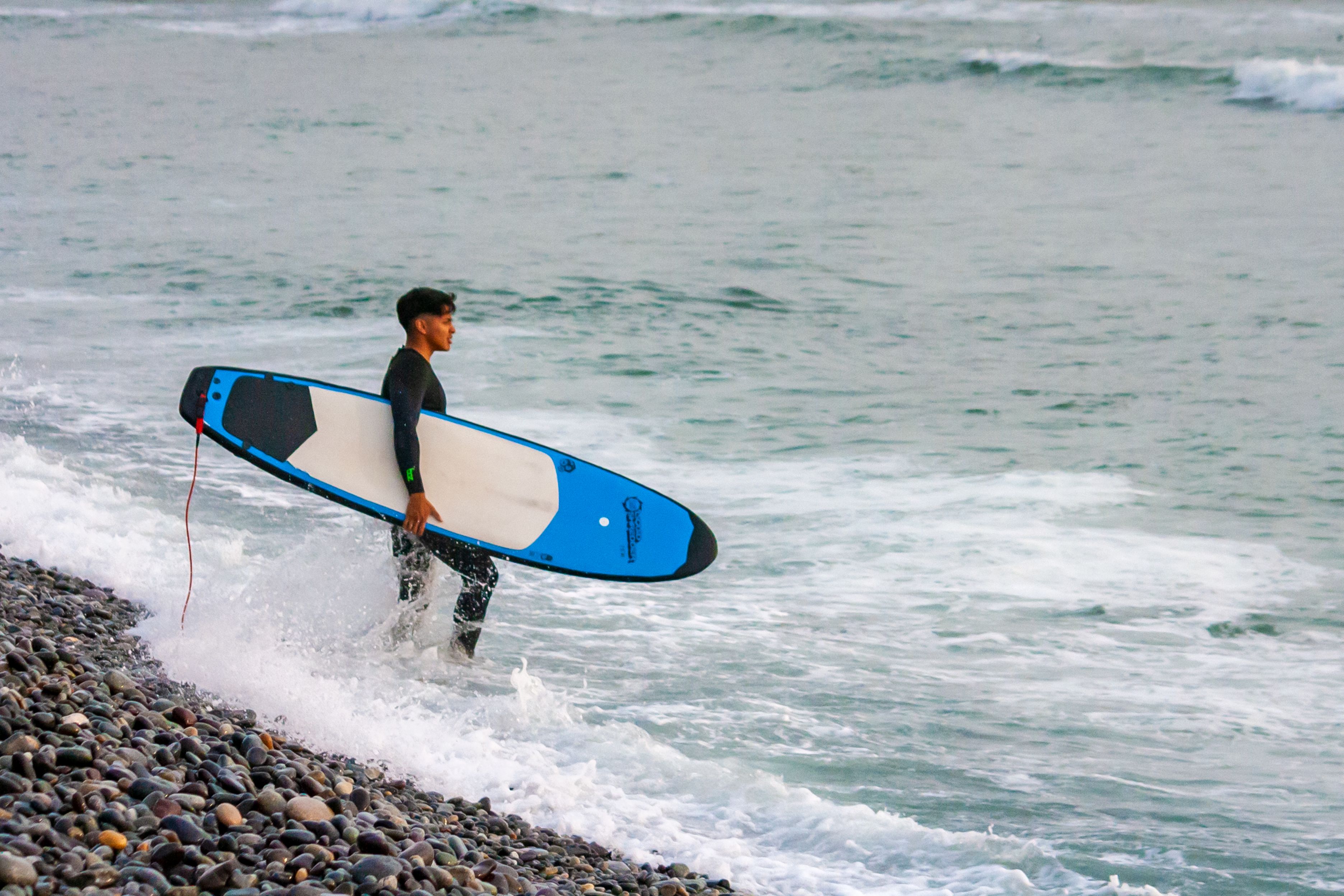 A surfer holding a surfboard on the rocky shores of Lima, Peru, ready for an ocean adventure.
