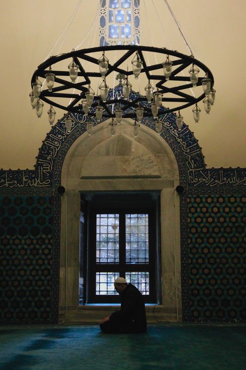 Free A serene interior featuring a man praying beneath an elaborate chandelier in a mosque with beautiful tiled walls. Stock Photo