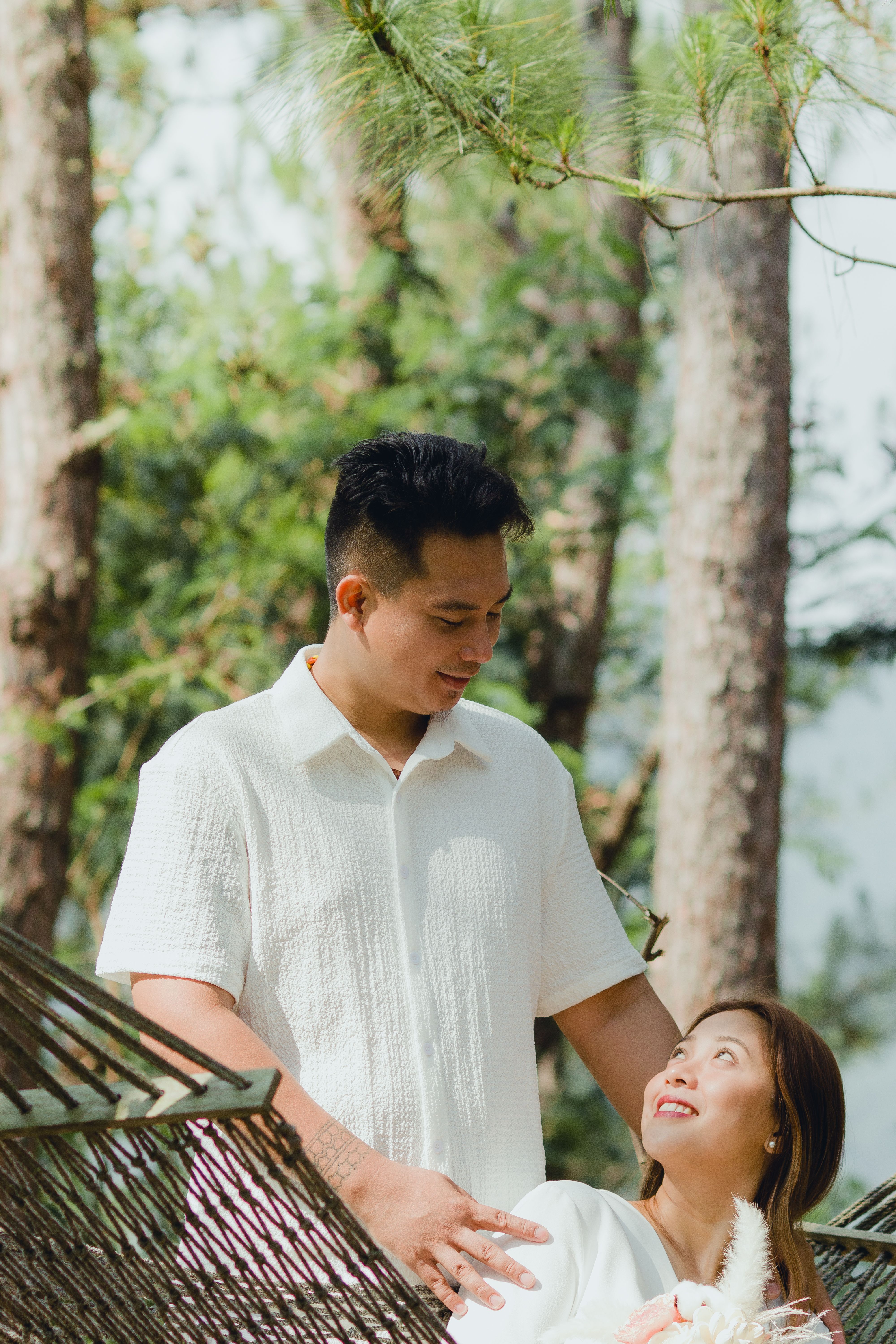 A person smiling and looking peaceful while sitting in a hammock in a forest.