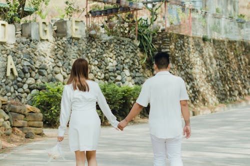 Back View of a Couple Holding Hands while Walking on a Pavement 