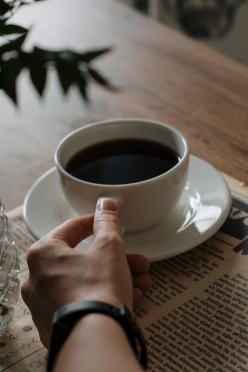 Free Hand holding a coffee cup next to a newspaper, perfect for a calm morning. Stock Photo