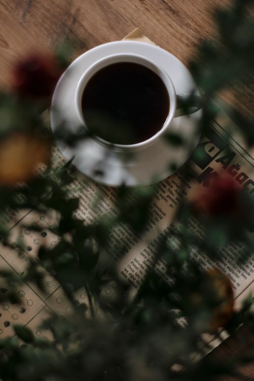 Free Top view of a coffee cup on a vintage newspaper with flowers in soft focus. Perfect for lifestyle themes. Stock Photo