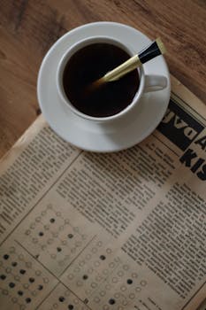 A classic vintage still life featuring a cup of coffee and an old newspaper.