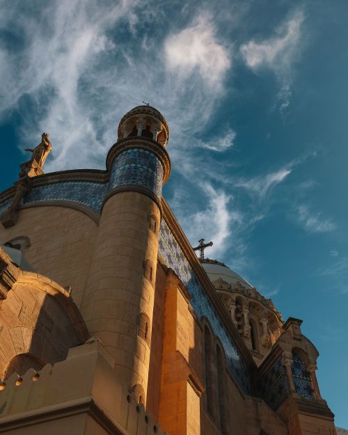 Free Low angle view of ornate architecture with cross silhouetted against a vibrant blue sky. Stock Photo