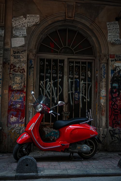 Free A striking red scooter parked in front of a graffiti-covered urban wall, capturing city life. Stock Photo