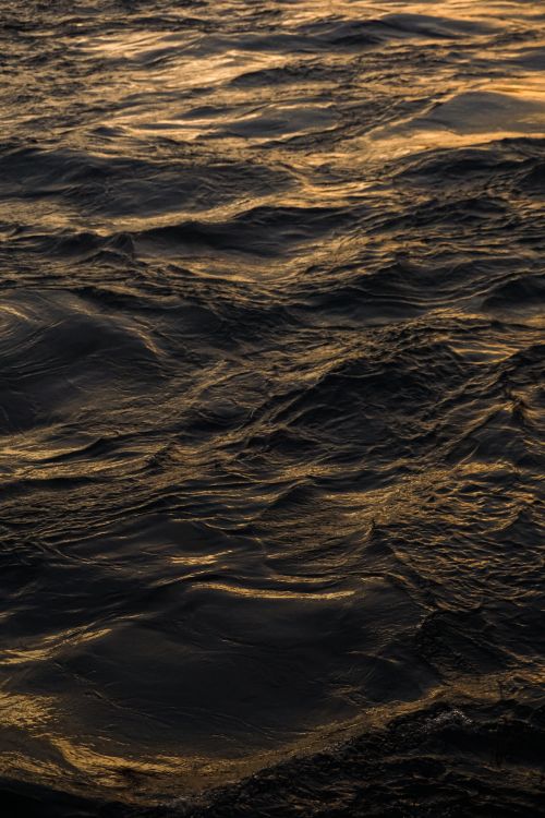 Free Captivating ocean waves reflecting golden sunset hues, creating a serene maritime scene. Stock Photo