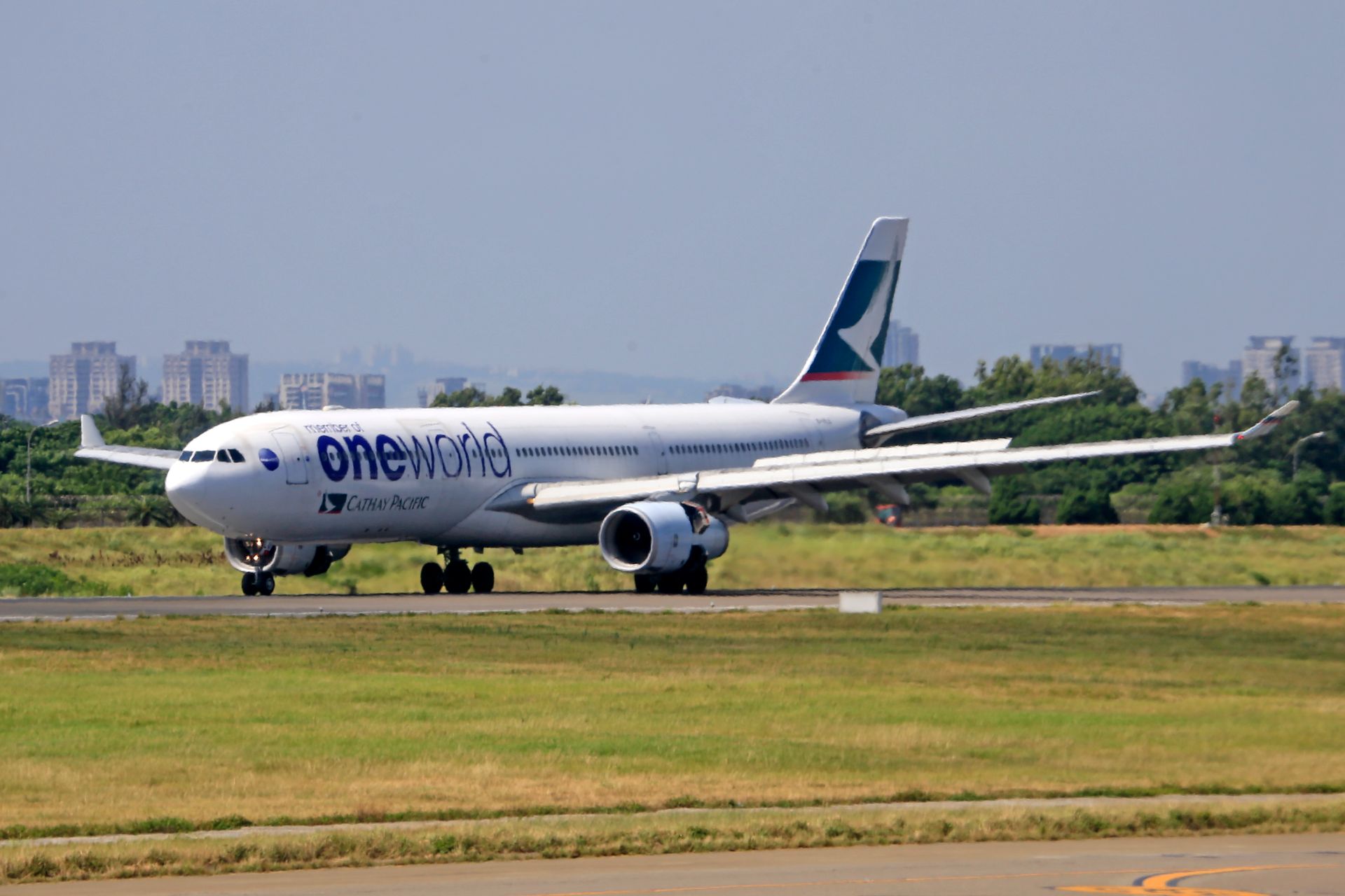 Cathay Pacific aircraft with oneworld livery on runway, ready for takeoff at airport.