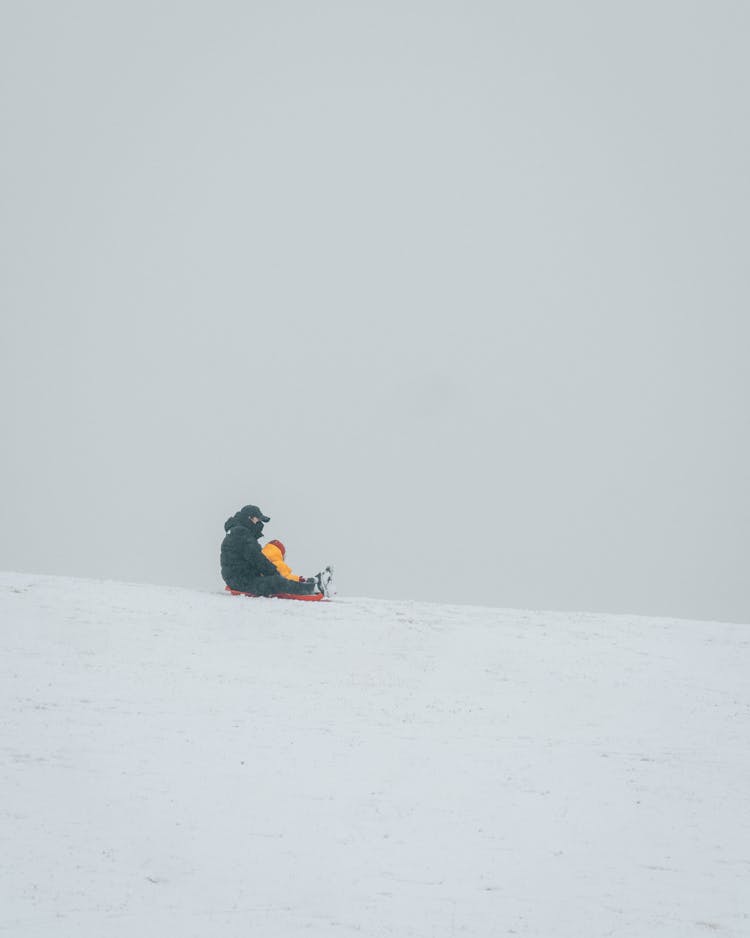 Parent Sitting With Child On Sleigh In Snow