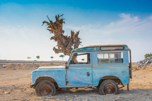 Free Old blue vintage car abandoned in a barren desert with a withered tree, symbolizing decay. Stock Photo