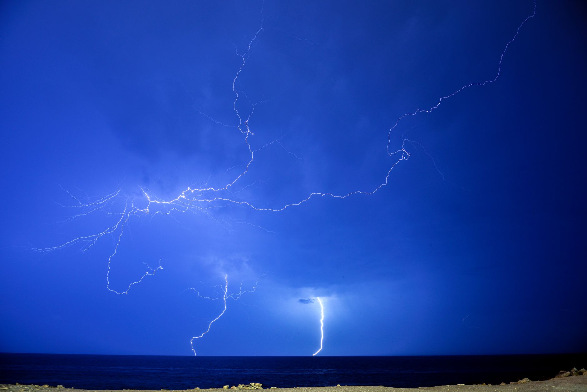 A stunning display of lightning bolts illuminating the night sky over a calm sea.