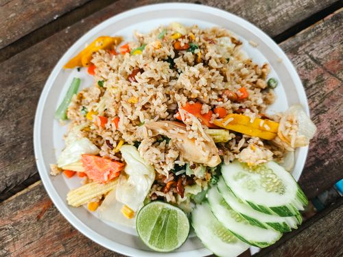 Free A vibrant plate of vegetable fried rice garnished with fresh cucumber slices and lime, perfect for a healthy meal. Stock Photo