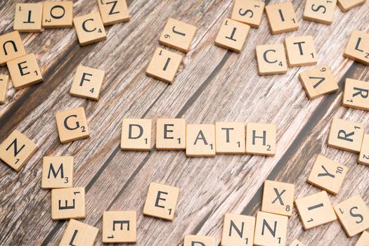 Wooden Scrabble tiles spelling 'Death' on a rustic surface, emphasizing themes of mortality.