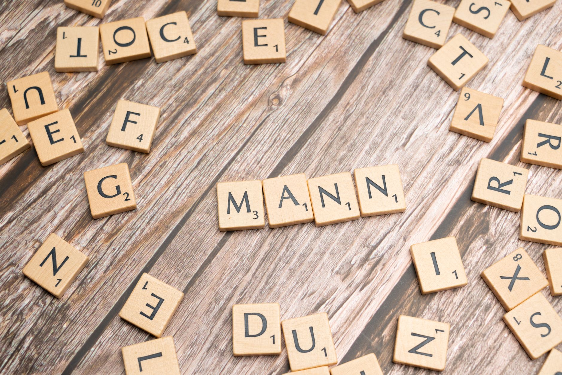 Wooden letter tiles forming the word 'MANN' on a rustic wooden table background.