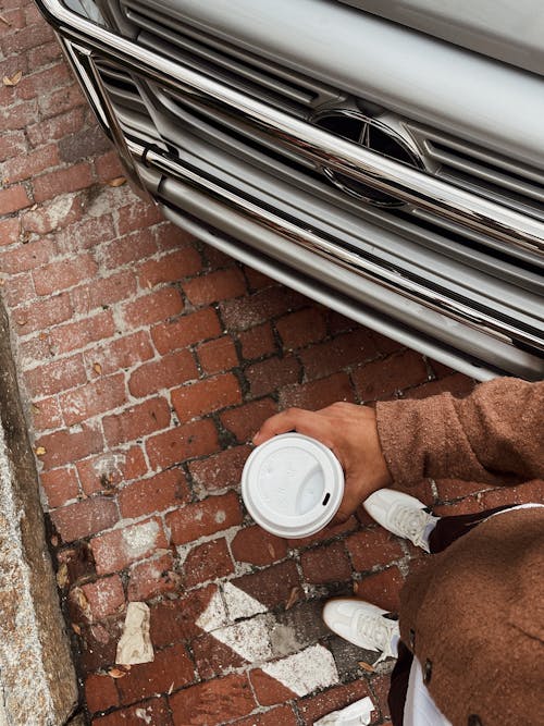 First Person Perspective of a Man Holding a Disposable Coffee Cup and Standing next to a Car