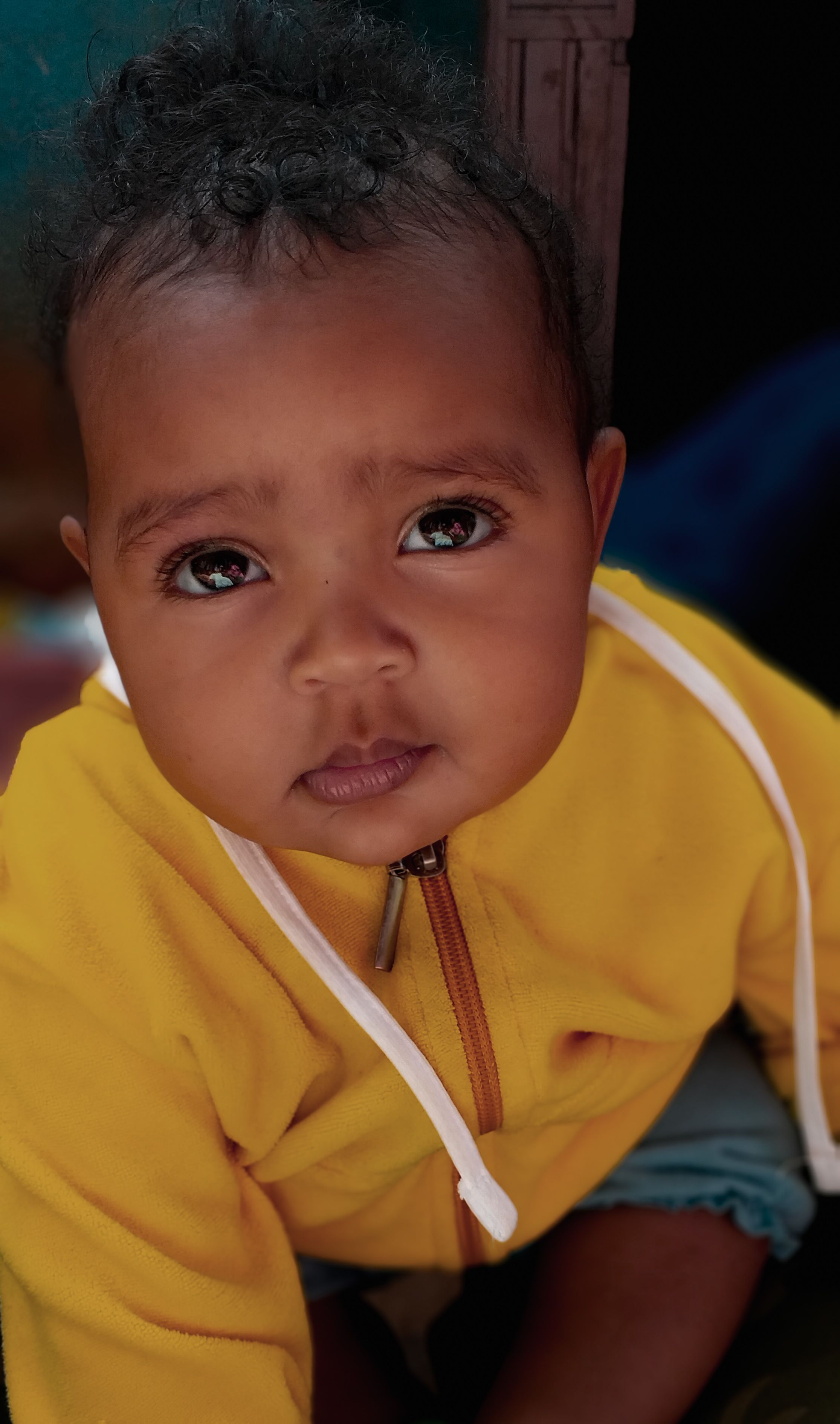 Charming portrait of a baby with black hair wearing a yellow hoodie, looking up.