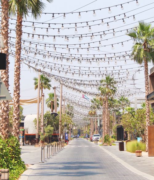 Free A picturesque Dubai street adorned with palm trees and hanging lights, capturing a vibrant summer day. Stock Photo