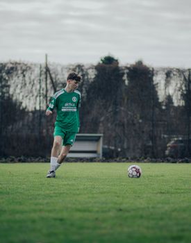 Young soccer player practices on a grassy pitch in Berlin, Germany, on a cloudy day.