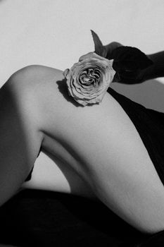 Elegant black and white image of a rose placed on a woman's leg, showcasing artistic minimalism.