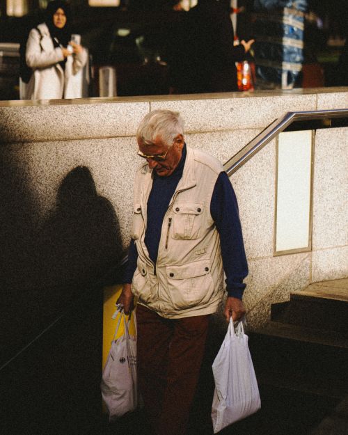 Free Senior man carrying shopping bags on city steps in Berlin, depicting urban life. Stock Photo