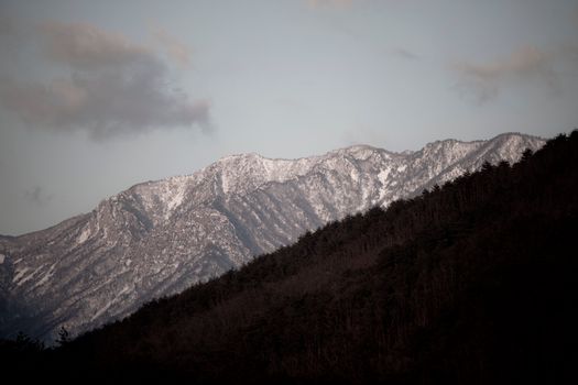 Scenic view of snow-capped mountains and forested hills under a twilight sky.