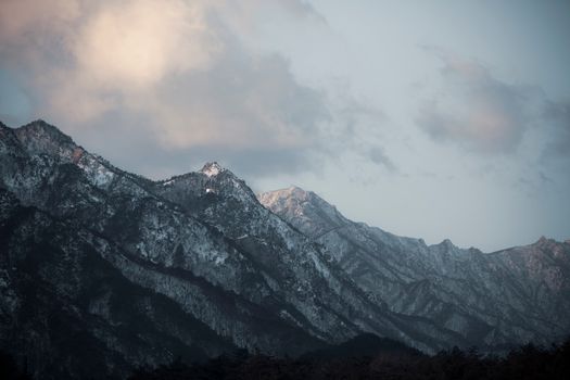 Stunning view of a snow-capped mountain range with clouds at dusk, capturing nature's beauty.