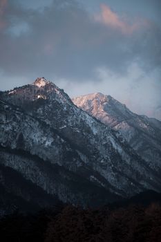 Stunning view of snow-covered mountain peaks with dramatic sky at sunset.