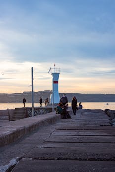 Beautiful sunset at İstanbul harbor with a lighthouse and people strolling along the pier.