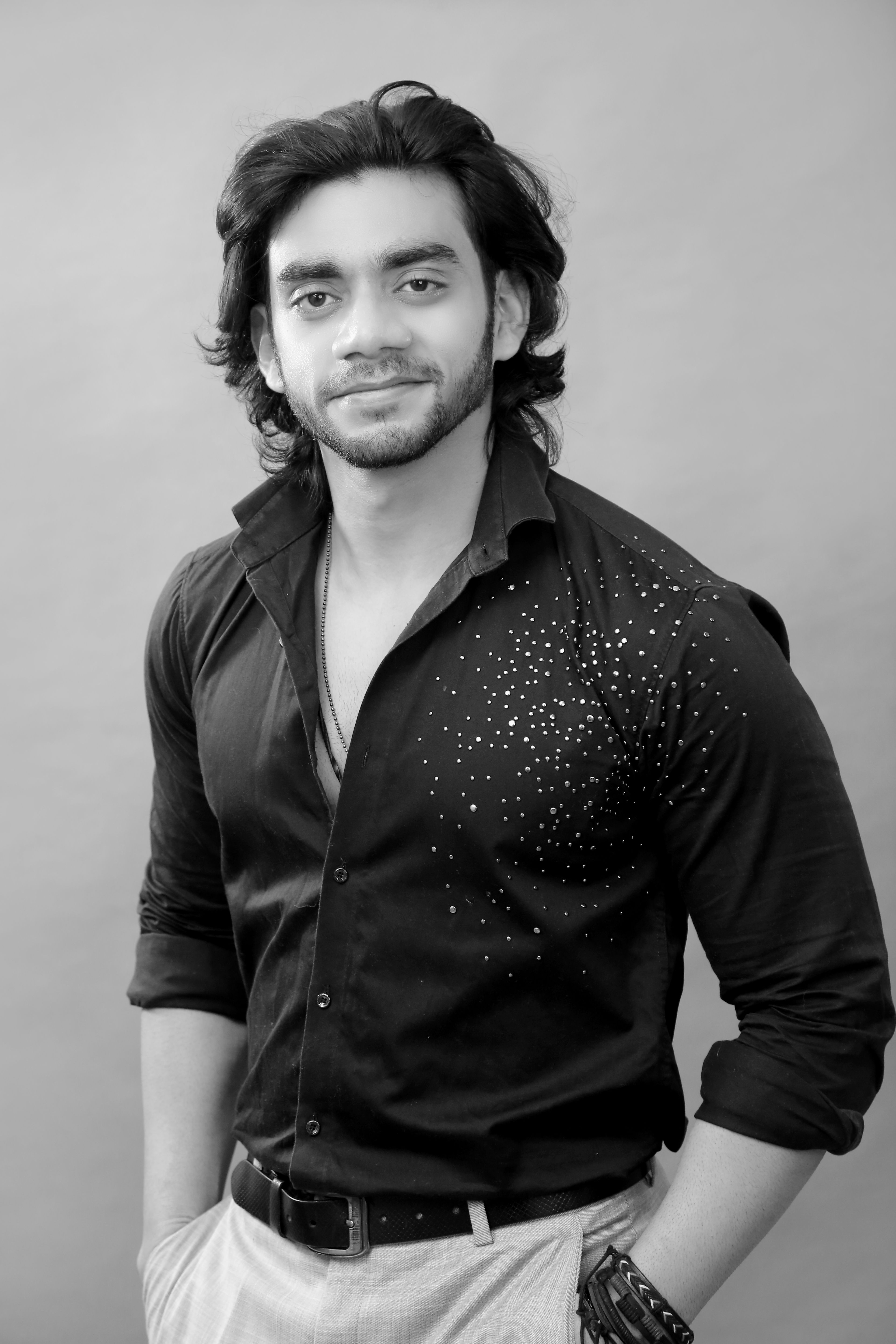 Striking black and white portrait of a stylish man in a detailed shirt, hands in pockets.
