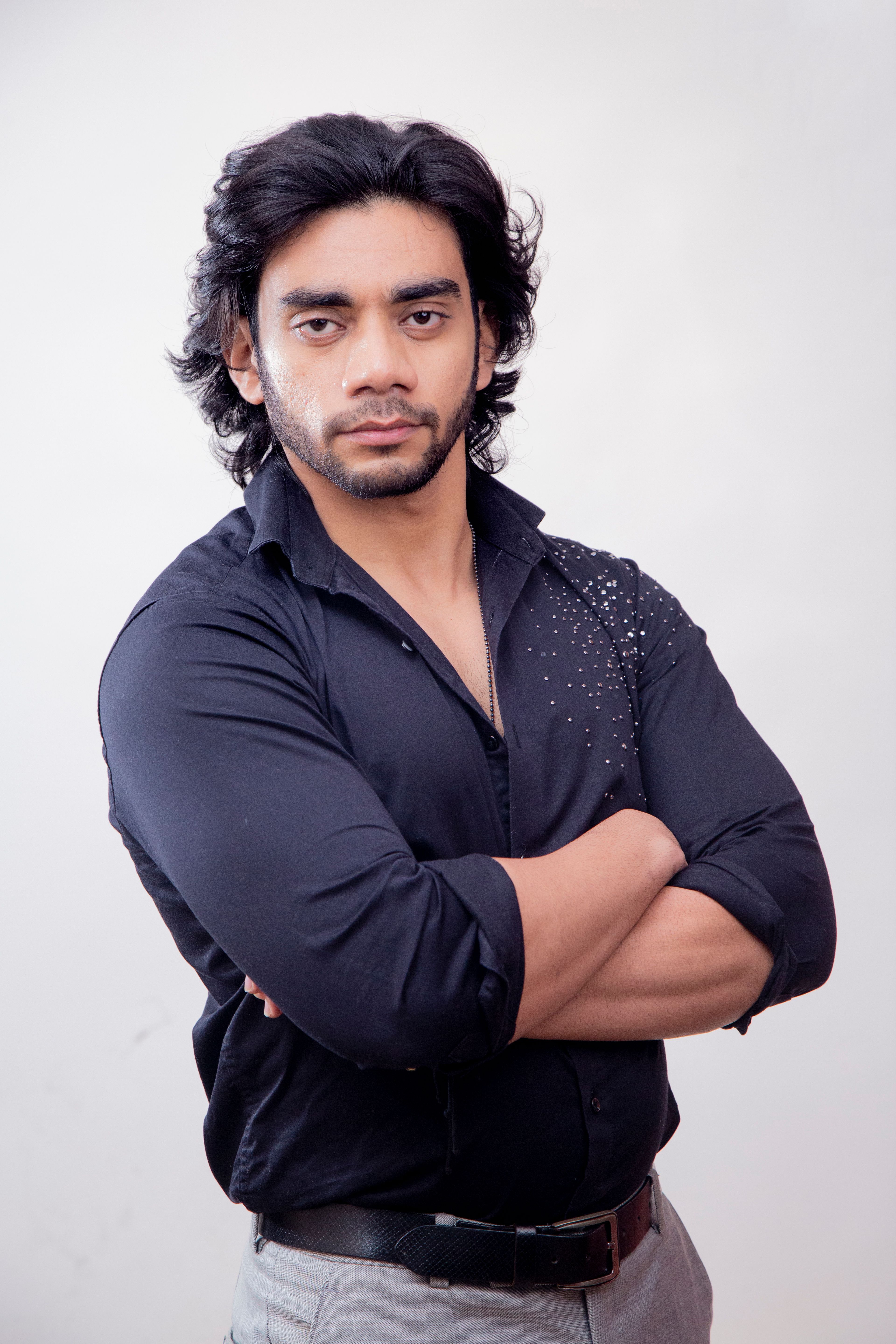 Portrait of a confident male model posing with arms crossed against a white background.