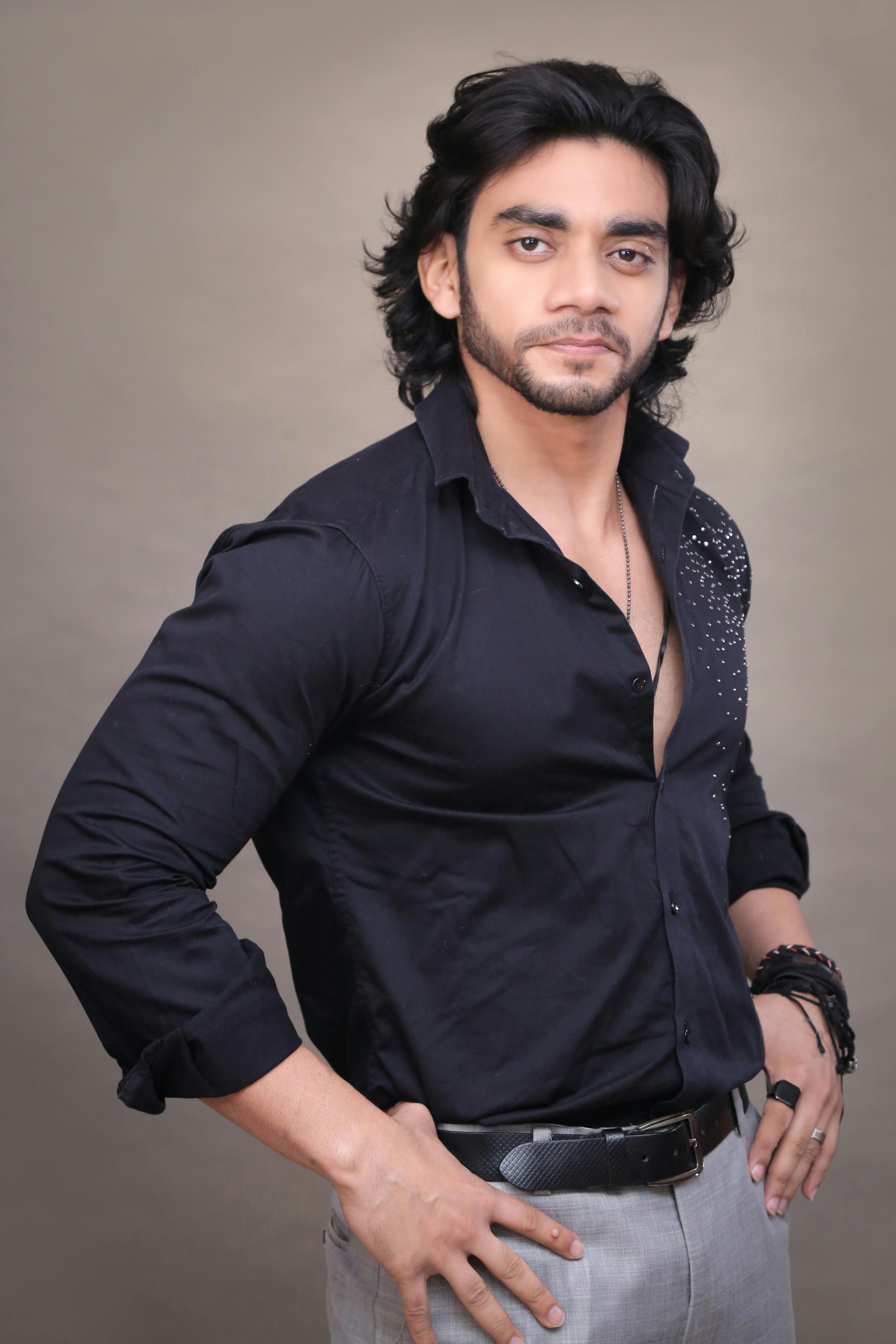 A confident man posing in a fashionable black shirt and gray pants, suitable for fashion and portrait themes.