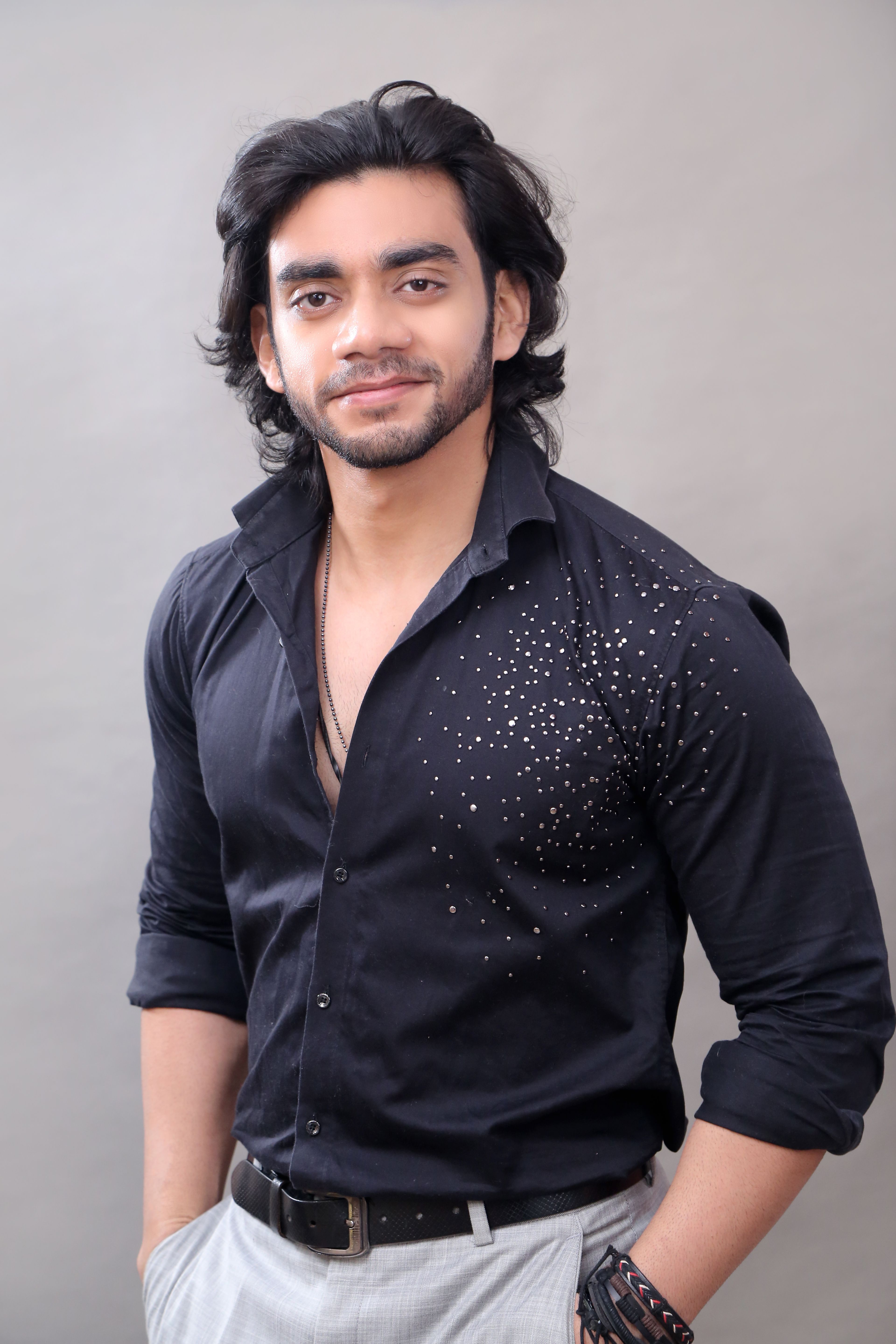 Elegant portrait of a smiling man in a stylish black shirt, hands in pockets, exuding confidence.