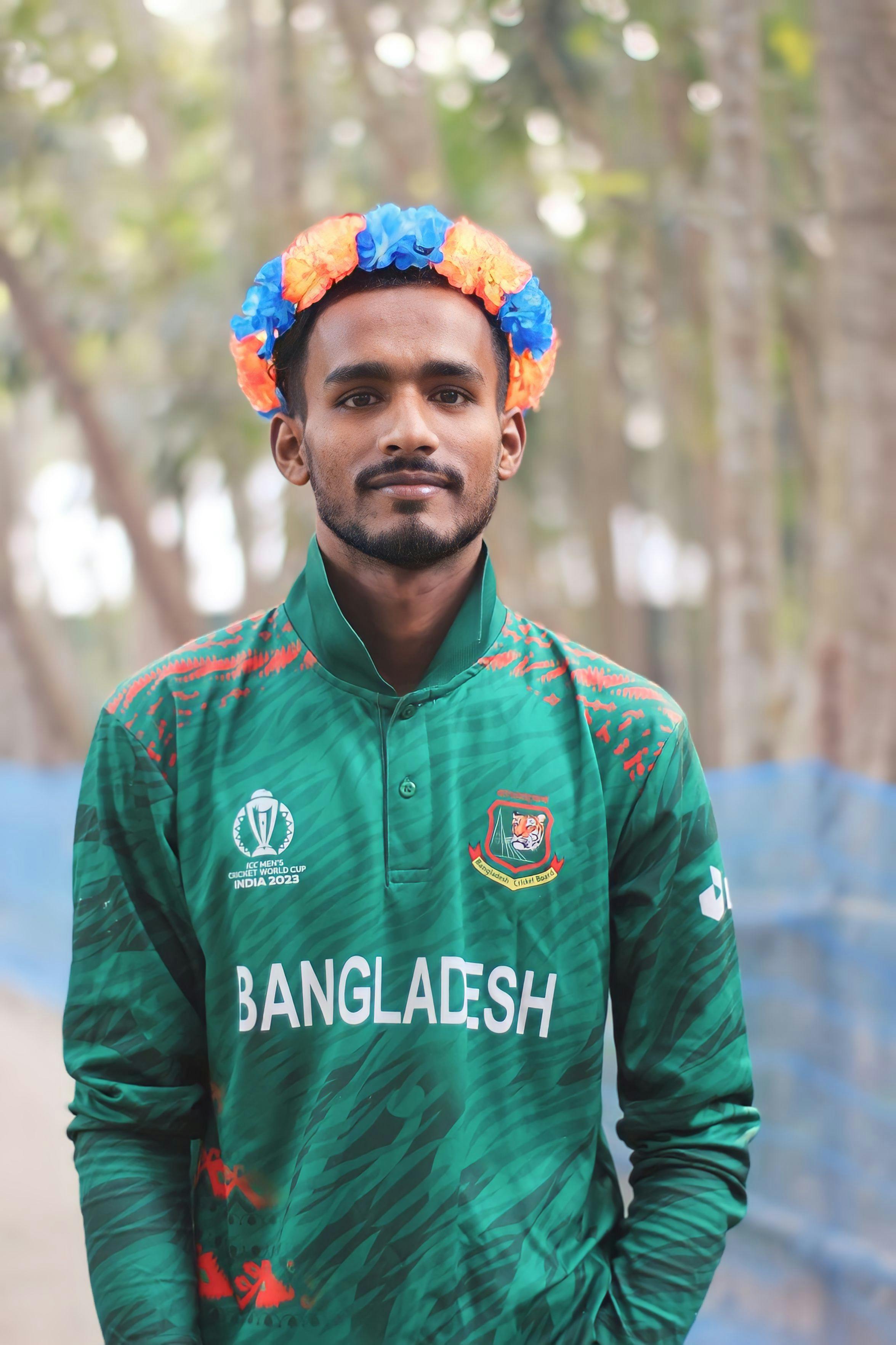 Portrait of a young man wearing a Bangladesh cricket shirt and floral crown outdoors.
