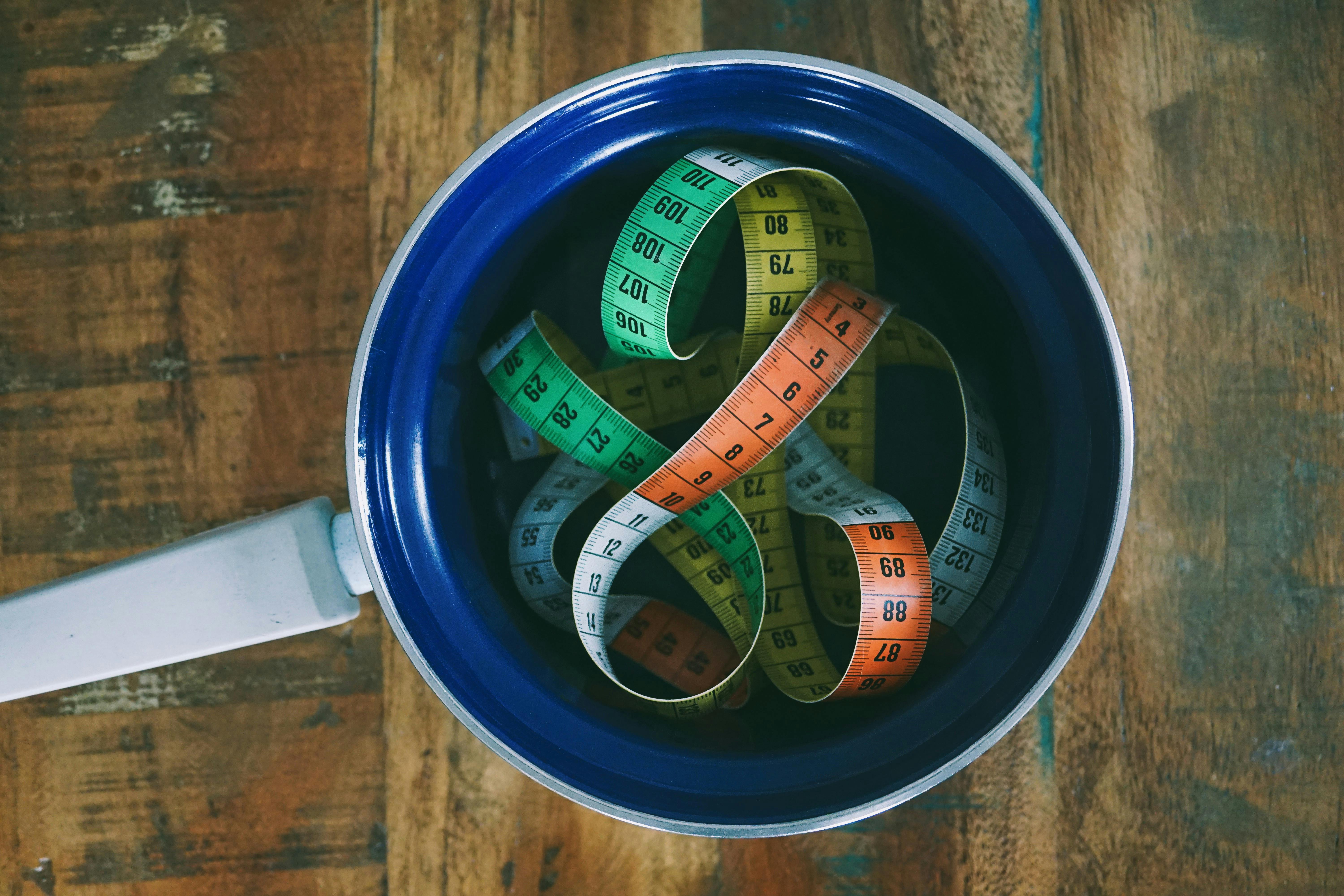 Top view of colorful measuring tapes in a ceramic pan placed on a rustic wooden table.