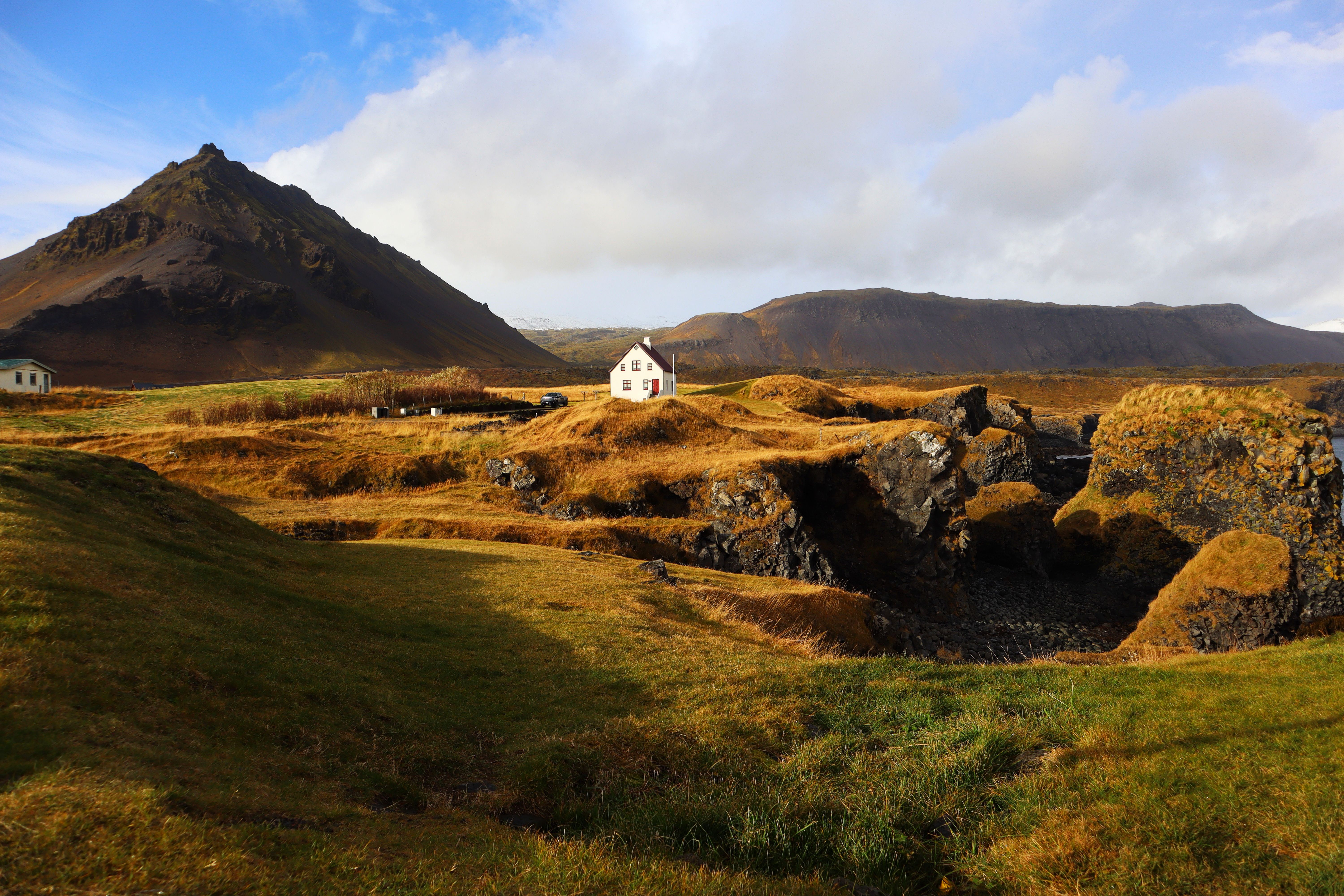 Beautiful rural landscape with mountain and house in Arnarstapi, Iceland, under a bright blue sky.