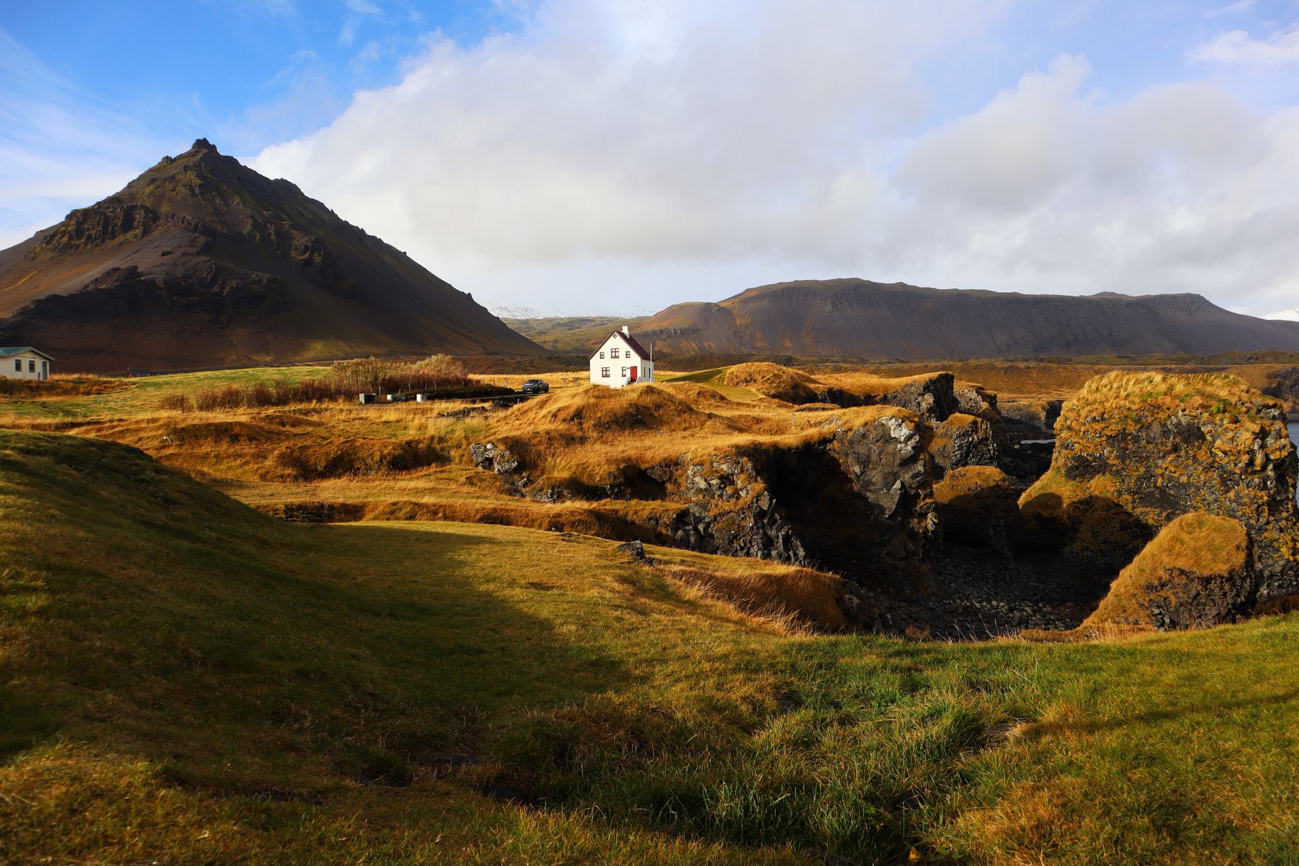Beautiful rural landscape with mountain and house in Arnarstapi, Iceland, under a bright blue sky.