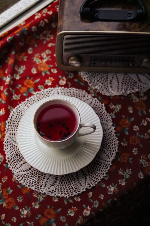 Free A vintage scene featuring a tea cup on a doily, accompanied by an old-fashioned radio on a floral tablecloth. Stock Photo