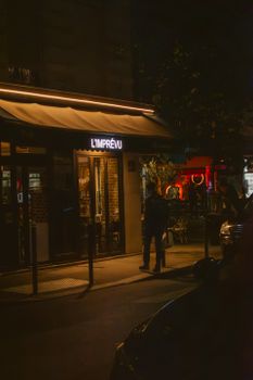 A man stands outside L'Imprévu restaurant at night, highlighting an urban nightlife scene.