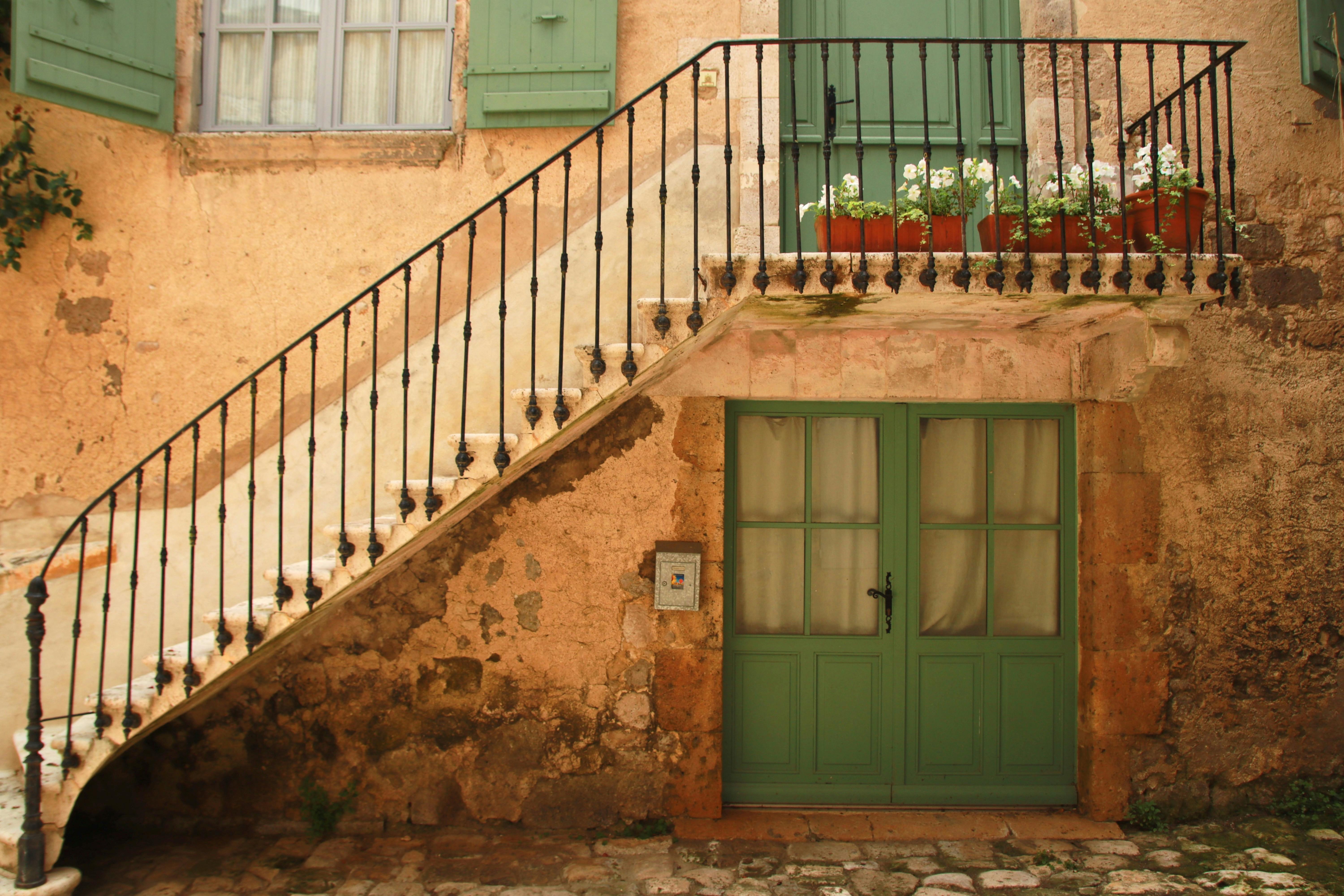 Rustic exterior of a French building with classic green doors and a staircase.