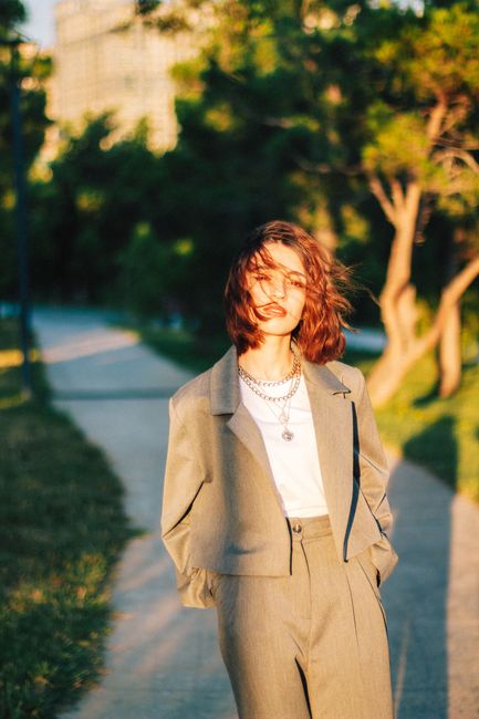 Elegant woman with brown hair walks confidently in a sunlit park, donning a chic suit.
