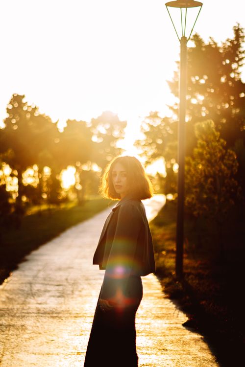 Free Elegant woman posing at sunset on a park path, creating a silhouette with sunlit background. Stock Photo