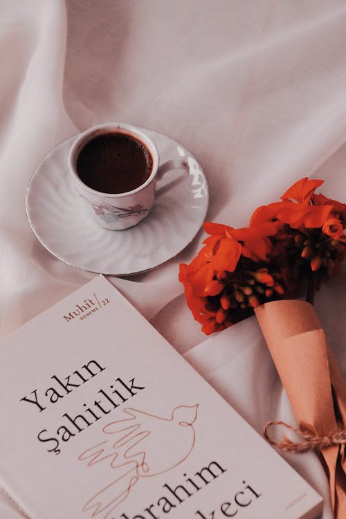 Cup of Coffee and a Bouquet of Red Flowers Next to a Book